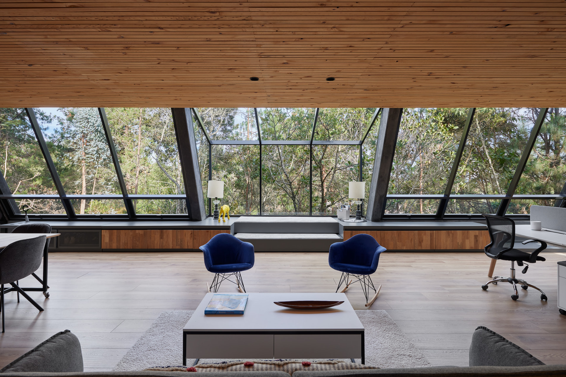 Sala de La Madriguera con muro de ventanales angulados y techo de madera