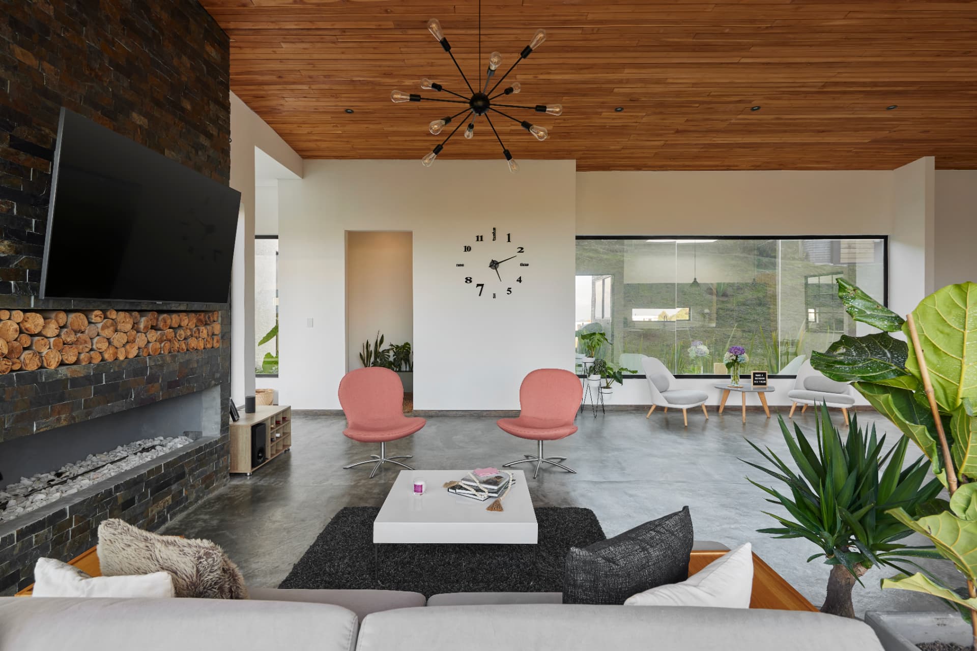 Sala de Casa MS con techo de madera, chimenea de piedra y ventanal al jardín