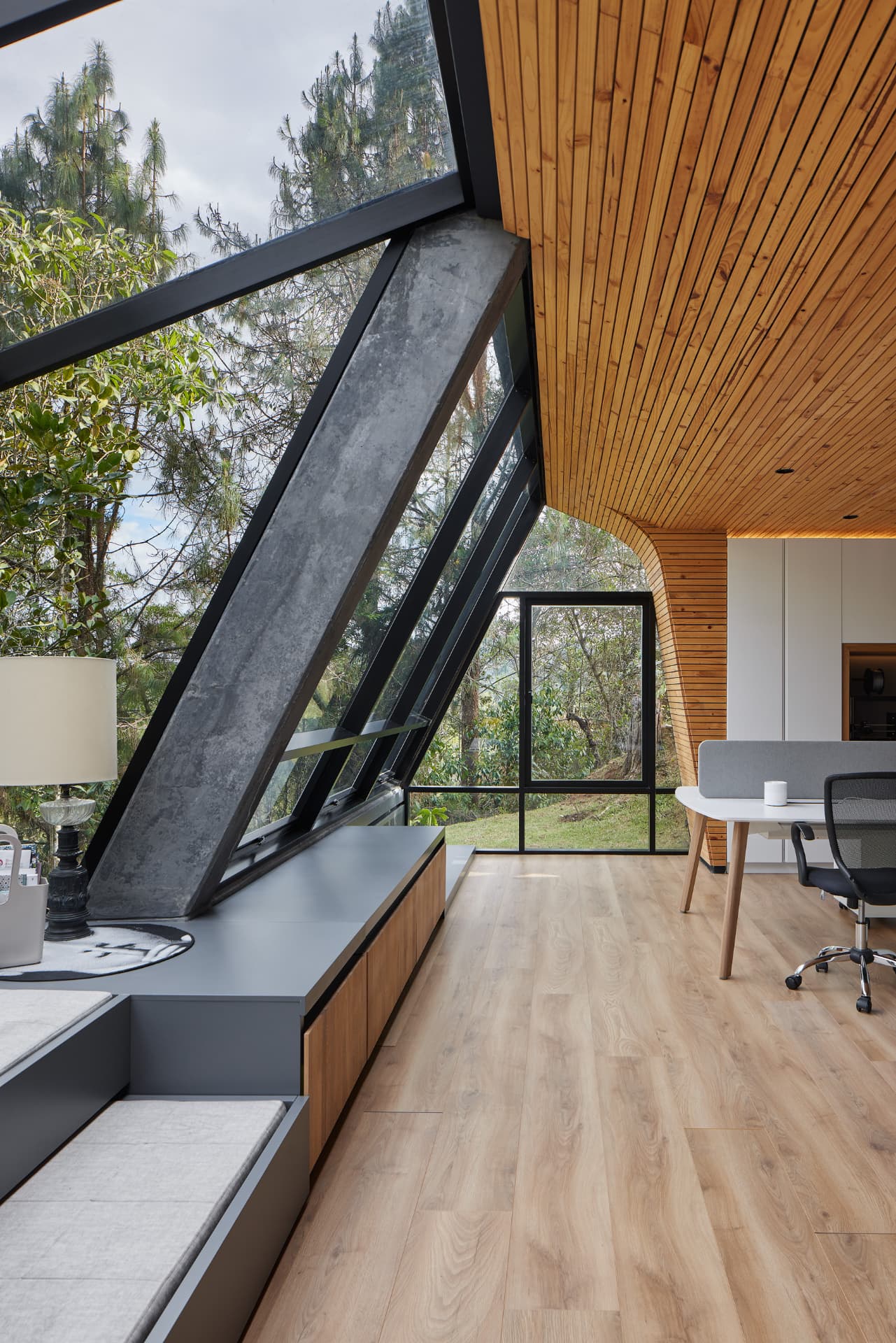 Interior de La Madriguera con techo curvo de madera y ventanal inclinado al bosque