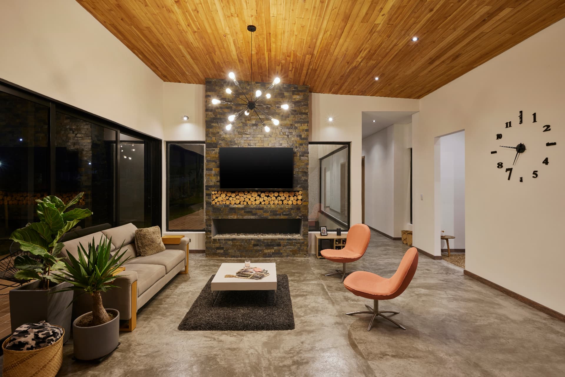 Sala de Casa MS de noche con chimenea, lámpara sputnik y reloj de pared